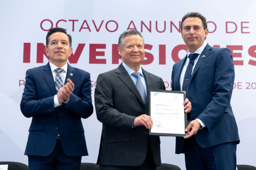 El gobernador de Hidalgo, Julio Menchaca Salazar, recibe un documento de inversión durante el Octavo Anuncio de Inversiones, acompañado por funcionarios estatales y representantes empresariales en Pachuca.