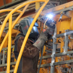 Trabajador realiza labores de soldadura en una estructura metálica dentro de una planta industrial, reflejando la actividad manufacturera en el sector industrial.
