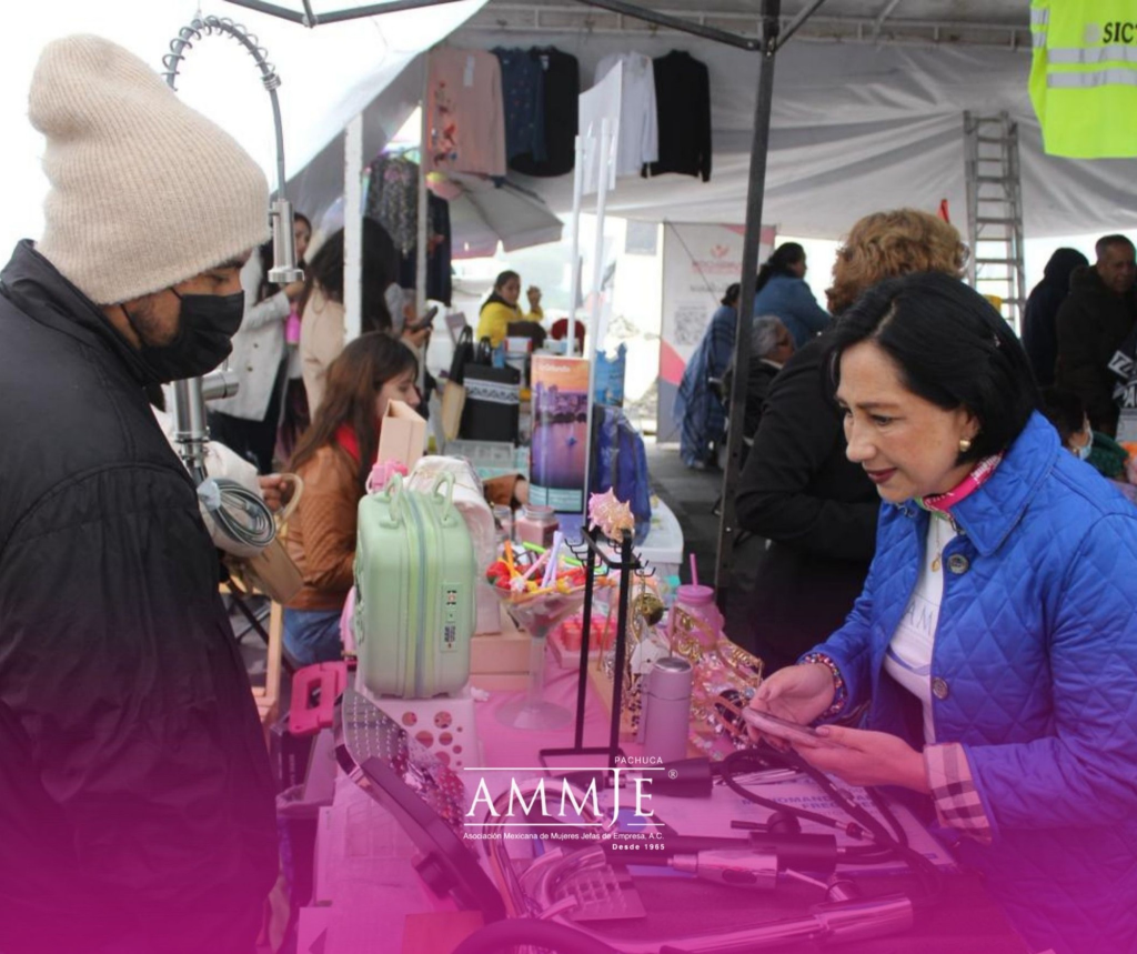 Mujer emprendedora muestra productos a una visitante durante la Feria del Emprendedor Inspira AMMJE en Mineral del Monte, en un espacio de venta y promoción de negocios locales.