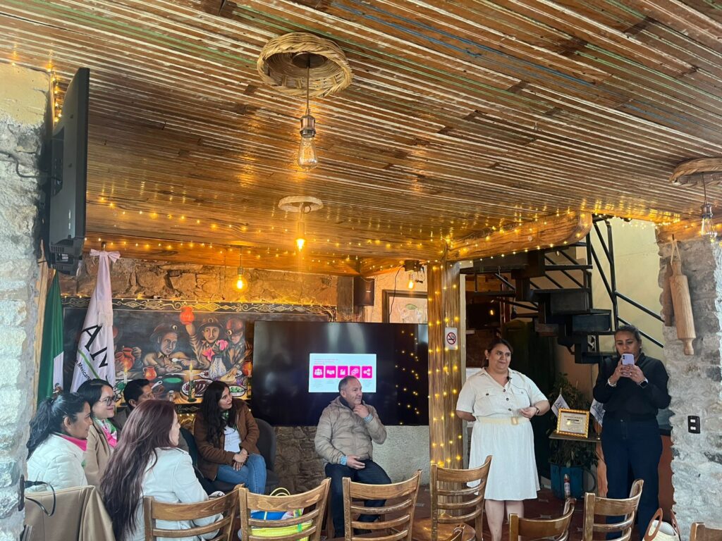 Personas participan en una charla sobre networking en un espacio interior rústico, con una expositora al frente y asistentes sentados escuchando la presentación.