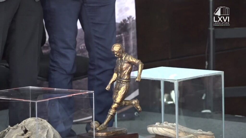 Escultura dorada de un futbolista junto a objetos históricos relacionados con el futbol en Real del Monte, exhibidos durante la presentación del proyecto para preservar el legado futbolístico del municipio.