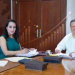 Julio Menchaca Salazar y Esther Ramírez Vargas durante una reunión de trabajo, en una composición ilustrada con gráficas de crecimiento y el mapa de Hidalgo.