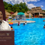 Elizabeth Quintanar Gómez durante la conferencia de prensa semanal del Gobierno de Hidalgo, junto a una imagen de familias y visitantes en un balneario.