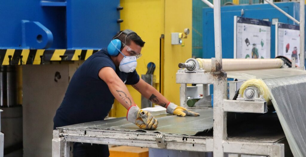 Trabajador con equipo de protección opera maquinaria en el área de producción de una planta industrial.