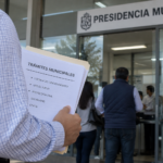Persona realiza trámites empresariales en una presidencia municipal, con documentos relacionados con licencias de funcionamiento, uso de suelo y Protección Civil.